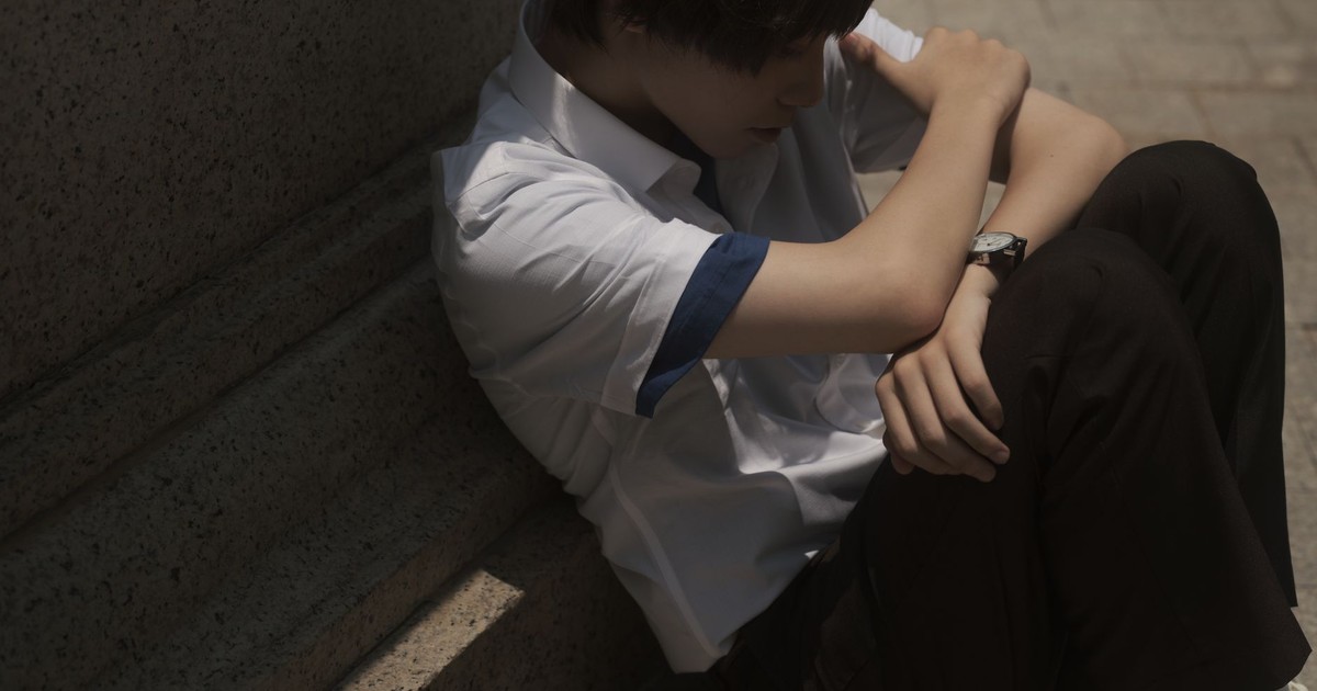 Teenager sitting thoughtfully on concrete steps, casting a shadow.