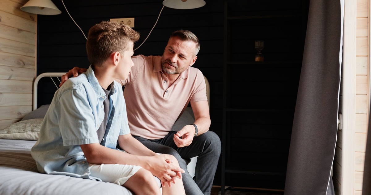 A father bonding with his teenage son in a cozy bedroom, sharing advice and conversation.