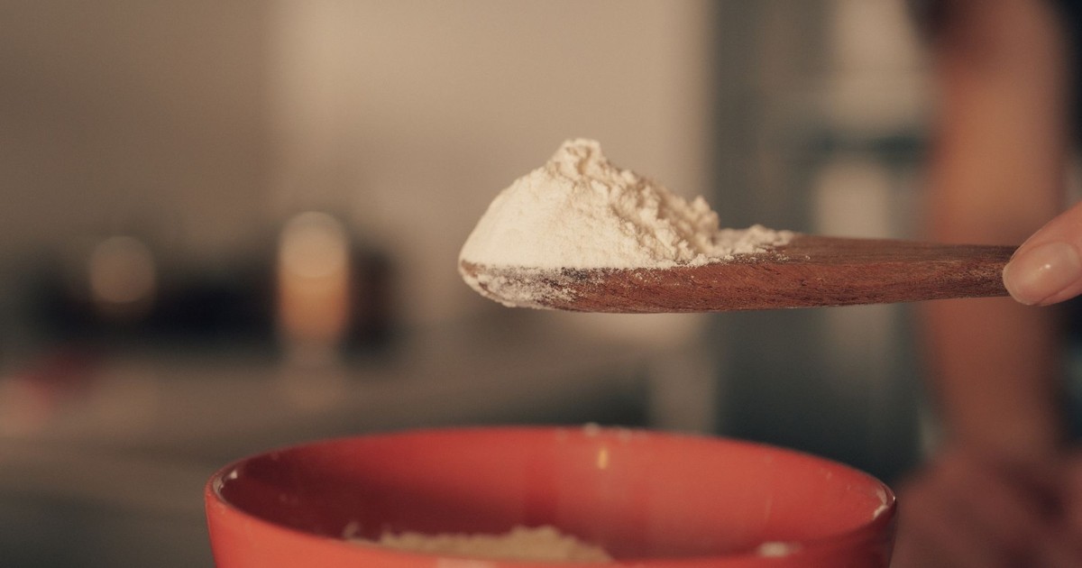 Close-up of flour on a wooden spoon over a red bowl in a kitchen.