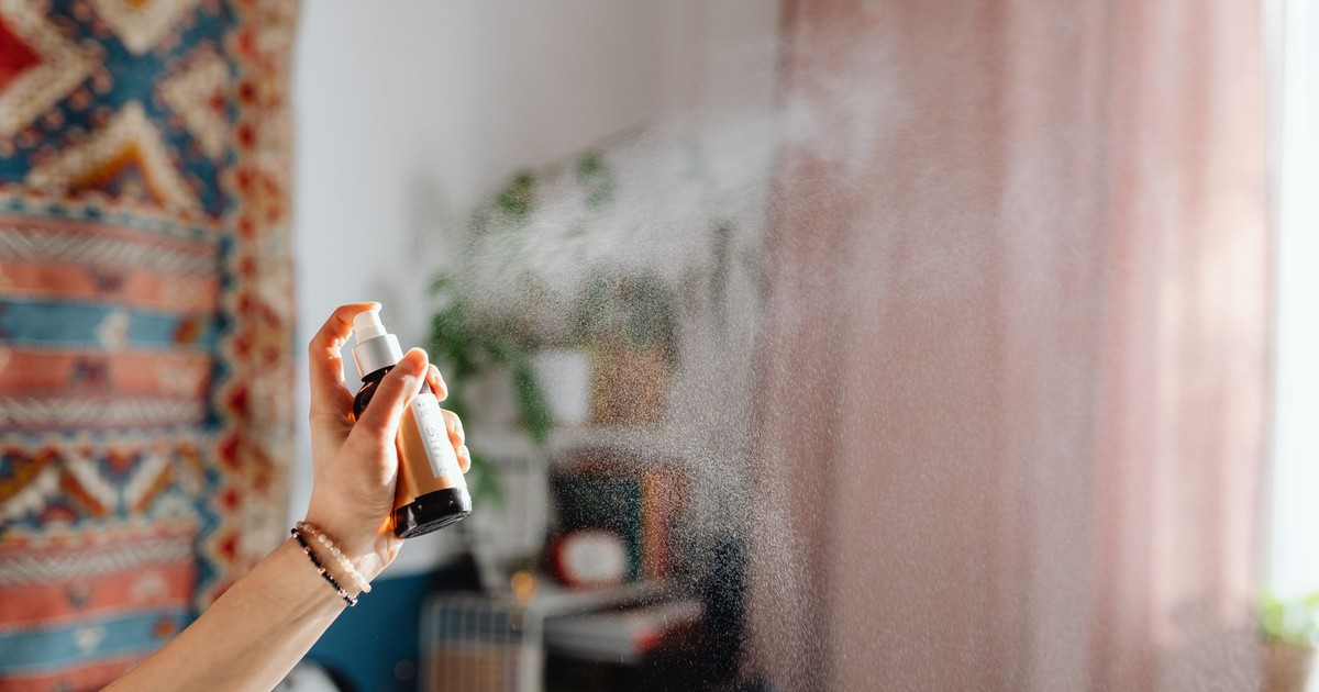 A hand spraying room freshener in a cozy home interior with ethnic decor and natural light.