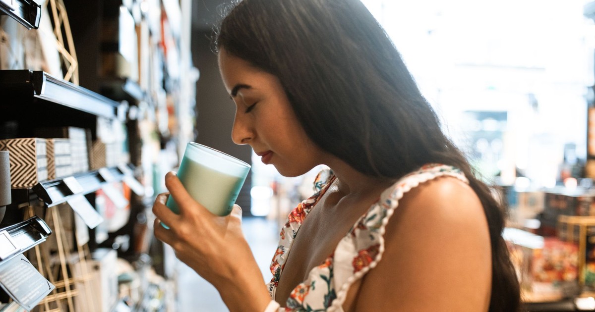 Young woman smelling a scented candle while shopping in a well-lit store.