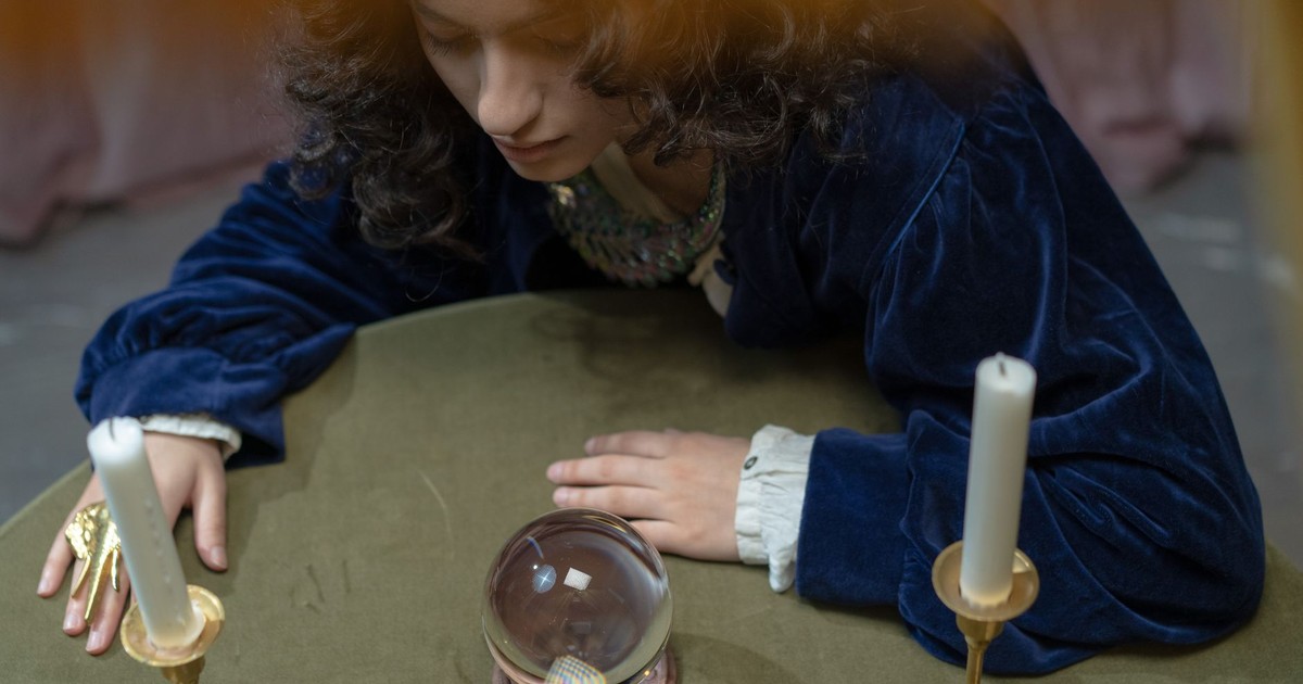 A fortune teller gazes into a crystal ball surrounded by candles and gems, creating a mystical atmosphere.