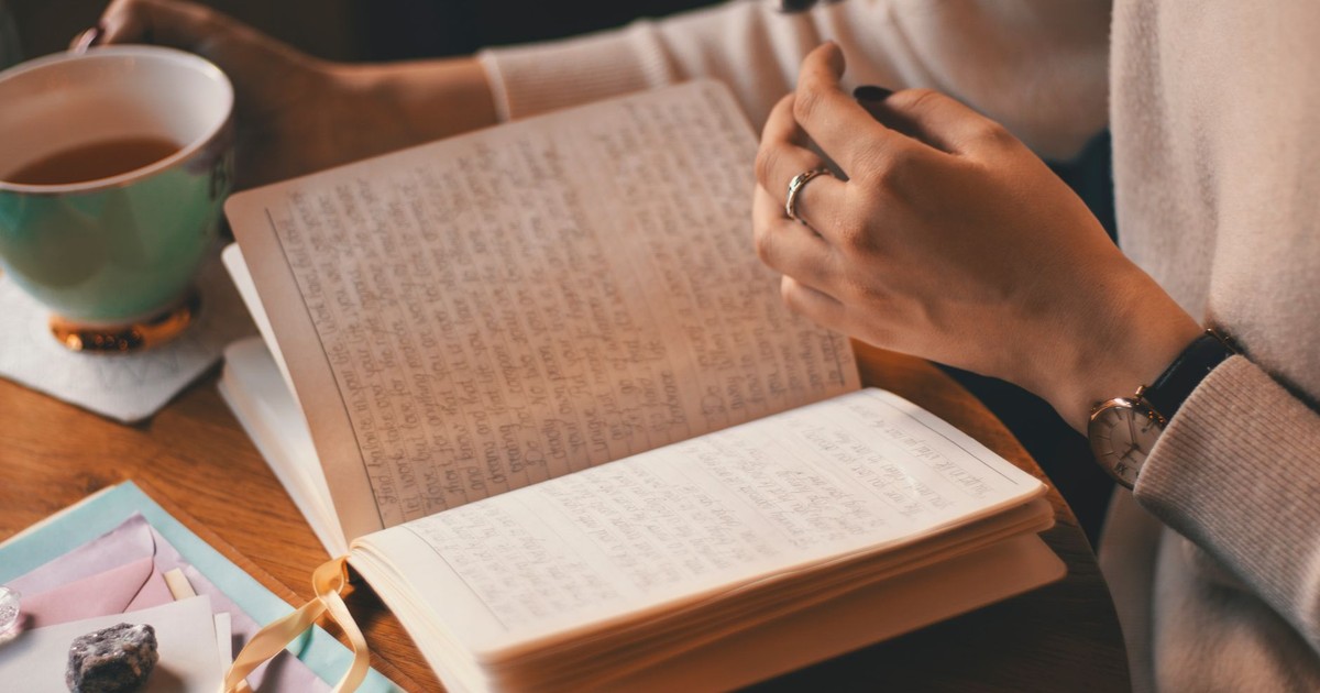 A woman writes in a journal while enjoying a cup of coffee at a wooden table.