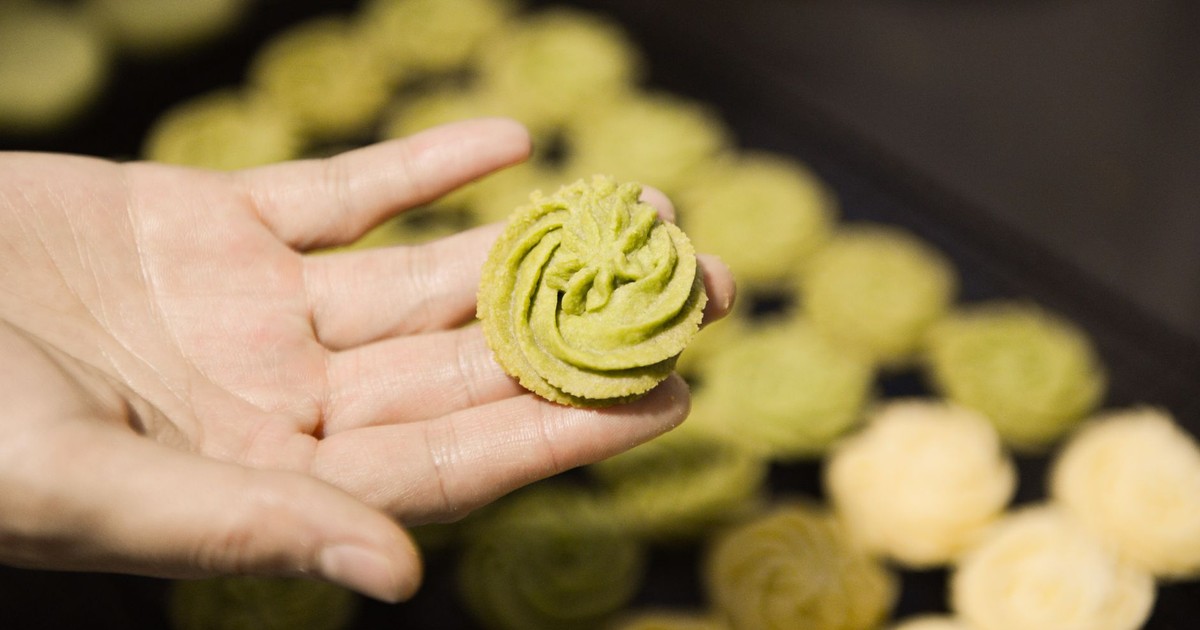 A close-up of a hand holding a green cookie, showcasing baked confections.