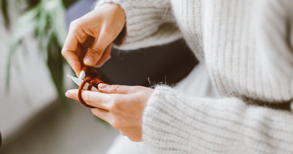 Hands engaged in knitting with yarn, creating a comforting woolen sweater indoors.