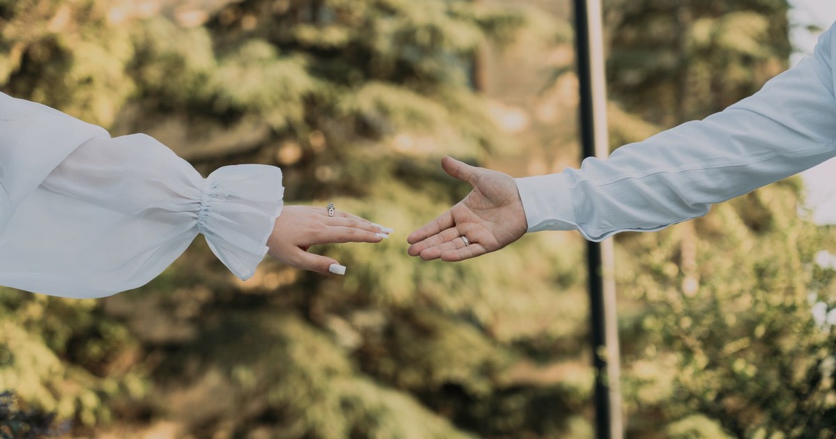 A man and woman reaching out to hold hands against a natural forest background.