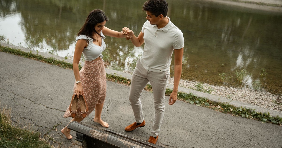 A couple walking hand in hand by a riverside park, enjoying a peaceful day outdoors.