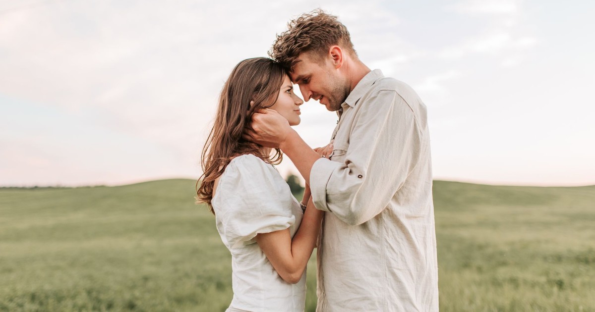 A loving couple embraces in a picturesque field during sunset, capturing a romantic moment.