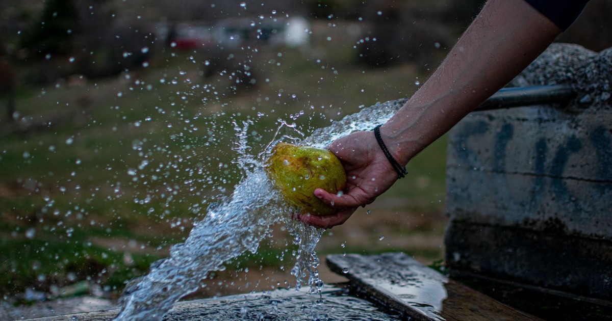 Person washing a pear under a running tap, capturing water splashing outdoors in Komnina, Greece.
