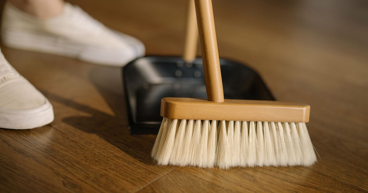 Close-up of a broom and dustpan with white sneakers indoors, representing housekeeping and cleanliness.