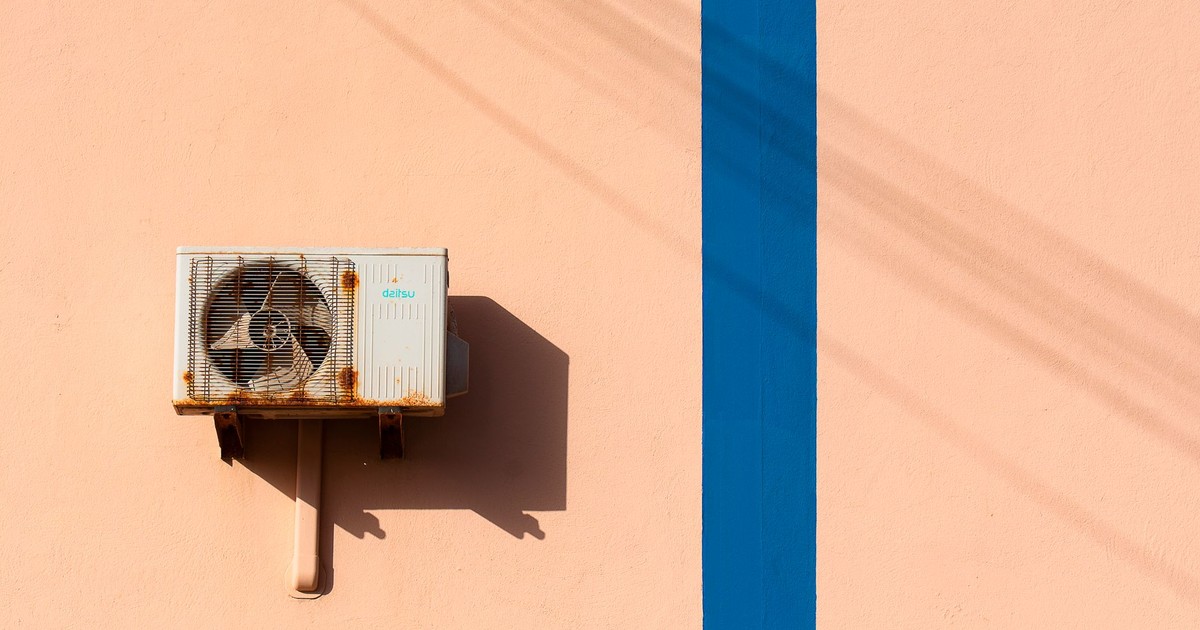 Rusty air conditioning unit casting shadow on a peach wall with blue stripe.