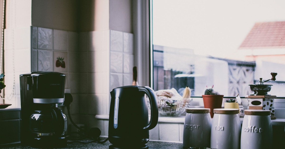 Cozy kitchen scene with coffee maker, kettle, and jars on a sunny counter.