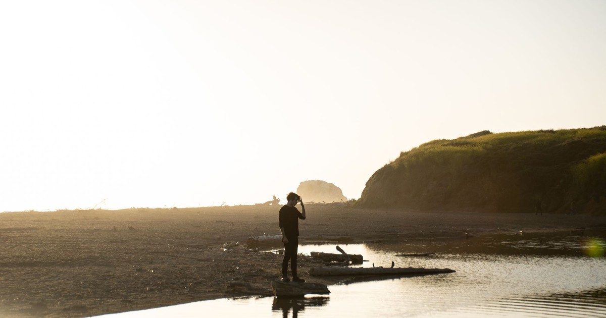 Silhouette of a man in black outfit standing on a coastal shore during sunset, capturing the natural beauty.