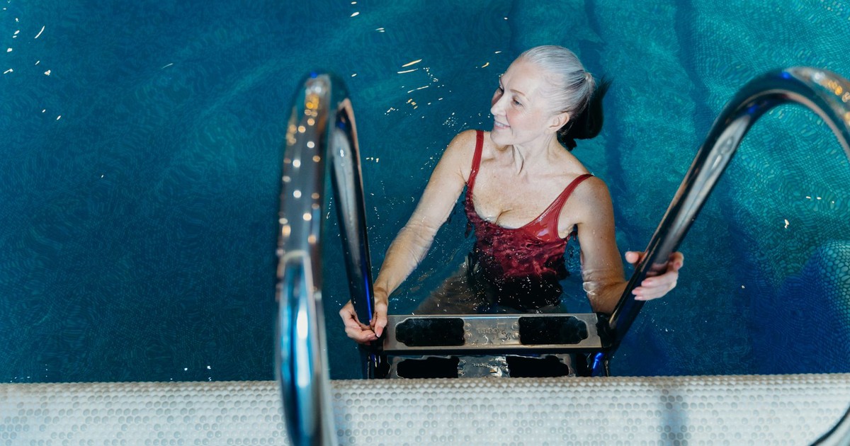 Elderly woman in a red swimsuit smiling while exiting a swimming pool.
