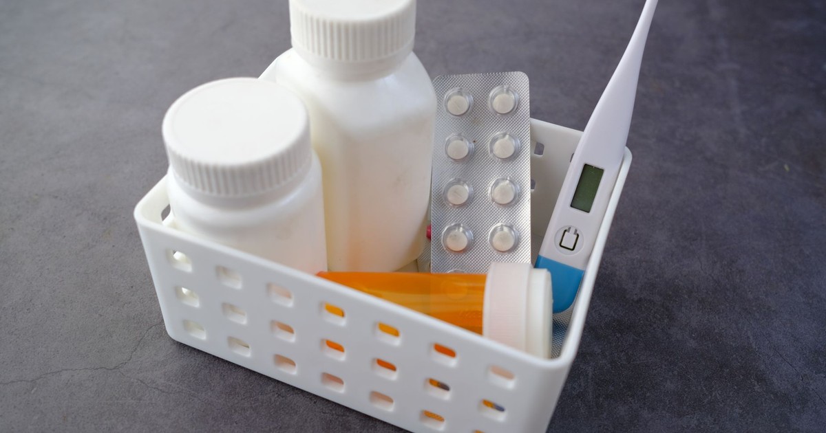 Healthcare basket with medication bottles, pills, and thermometer on a dark surface.