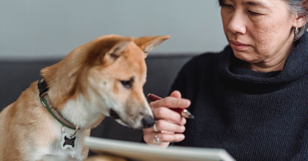 Close-up of a woman interacting with her dog while writing or drawing.