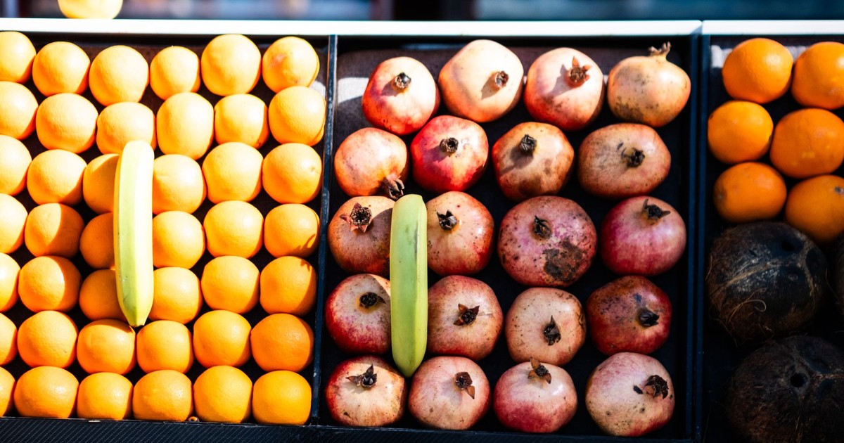 Colorful rows of fresh fruits including oranges, pomegranates, and bananas at a market.