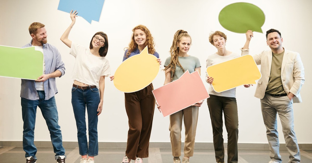 Diverse group of smiling adults holding vibrant speech bubbles indoors.