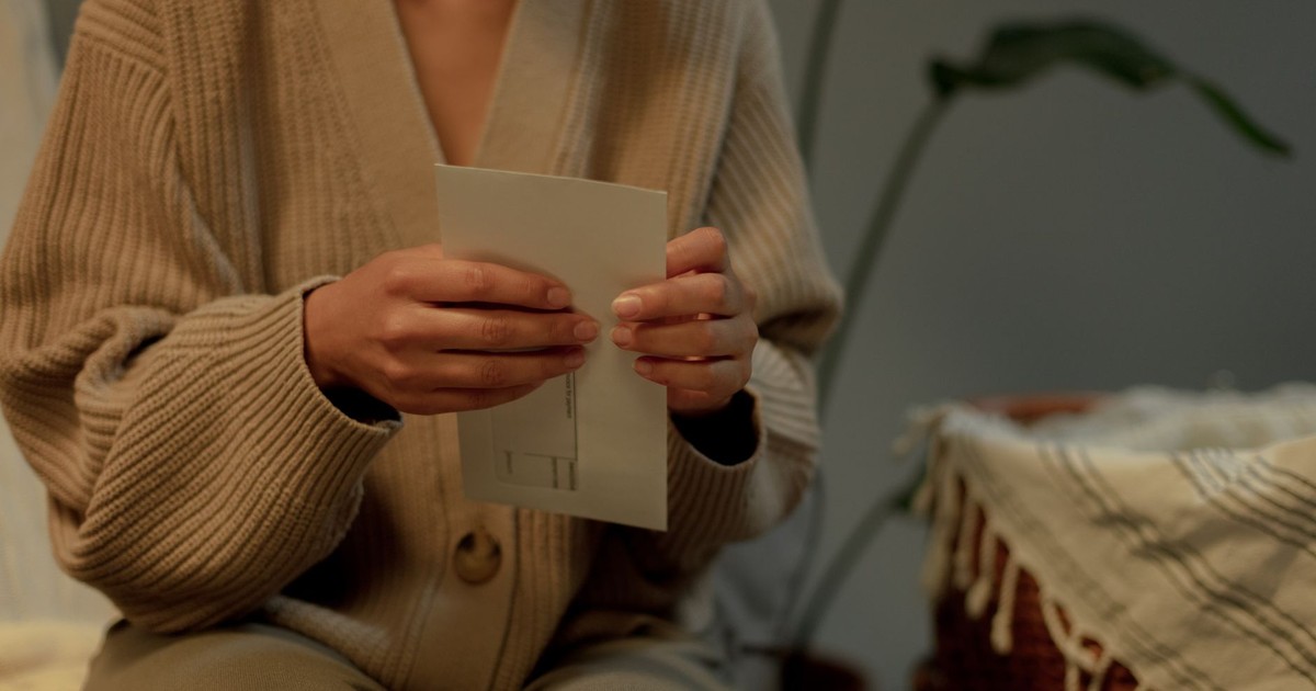 An adult holding a letter indoors, wearing a warm sweater, evoking a cozy mood.