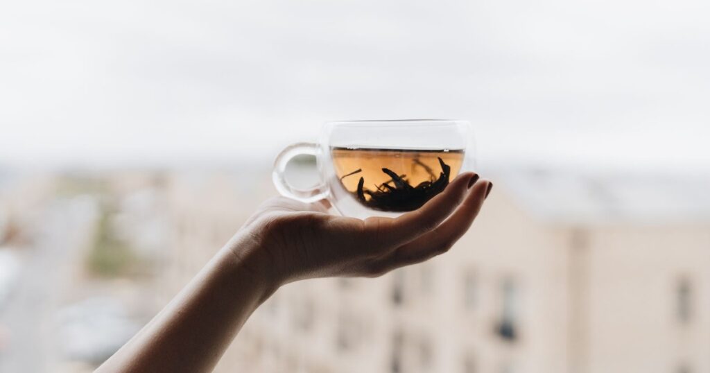 Hand holding a glass cup of tea with cityscape view, perfect for lifestyle and beverage themes.