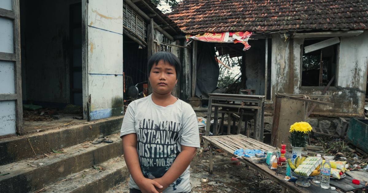 A young boy stands in front of a rustic house in Phú Yên, Vietnam, showcasing his surroundings.