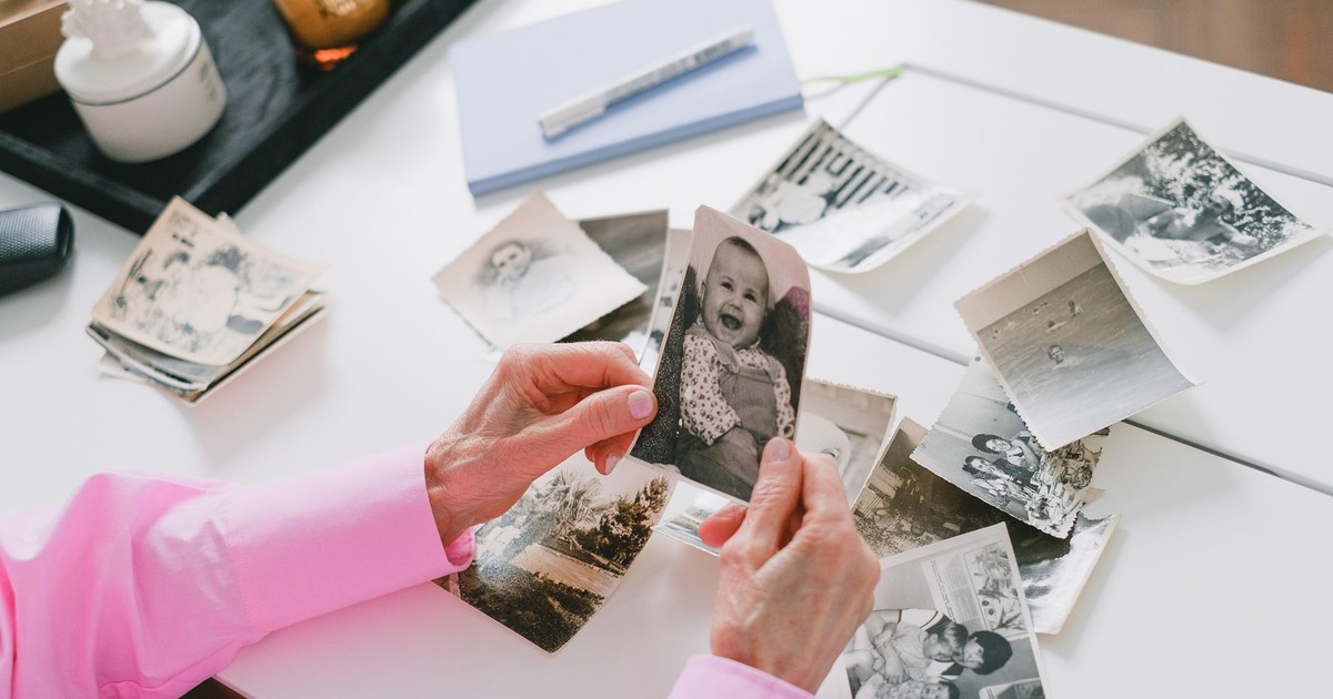 A person in a pink shirt organizing old black and white family photos on a table.