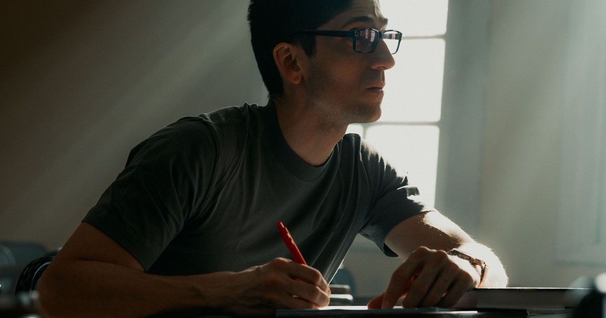 A young adult writing attentively in a classroom illuminated by soft sunlight.