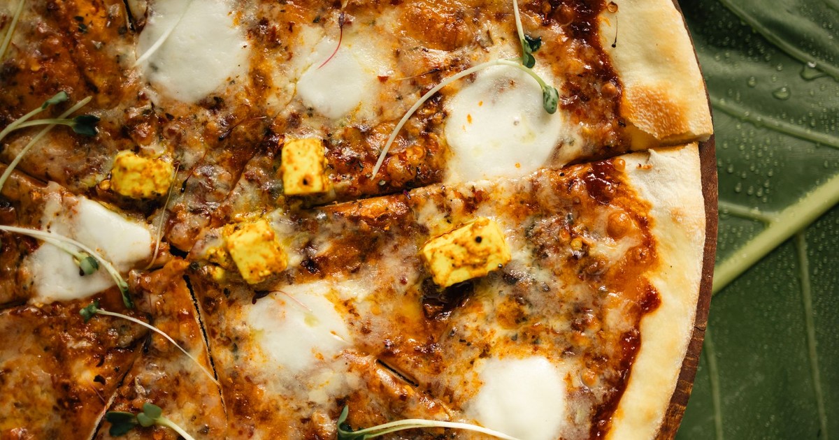 Close-up of a mouthwatering paneer pizza with fresh microgreens on a leaf background.
