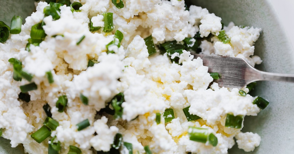 Top view of gray bowl with meal cottage cheese with pieces of green onion and fork placed on kitchen meal for breakfast