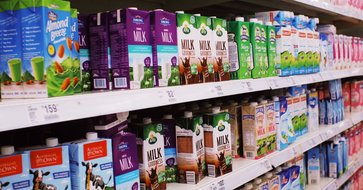 Various colorful boxes of milk placed on shelves with prices in modern supermarket