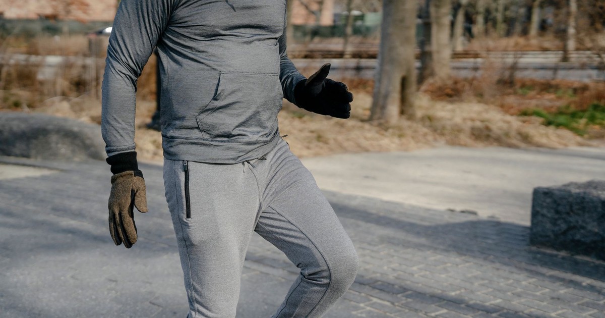 Crop anonymous male in sportswear and gloves jumping on one leg while warming up before workout training in city park