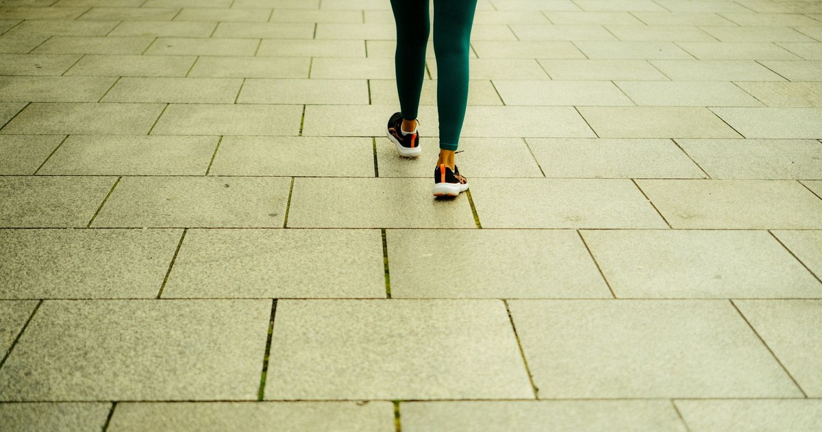 A person in green leggings walks on a stone tiled sidewalk in Dublin promoting a healthy lifestyle.
