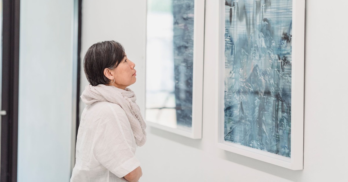 A woman attentively observes abstract paintings in an art gallery setting.