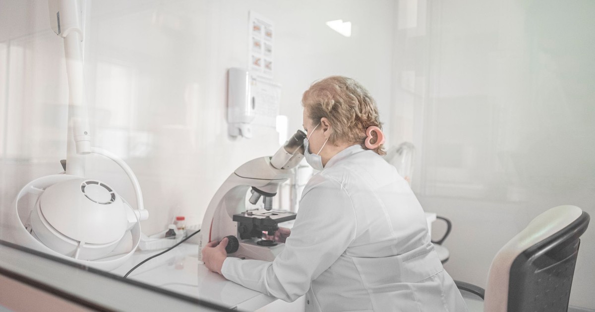 A scientist works with a microscope in a bright, modern lab setting, wearing a lab coat.