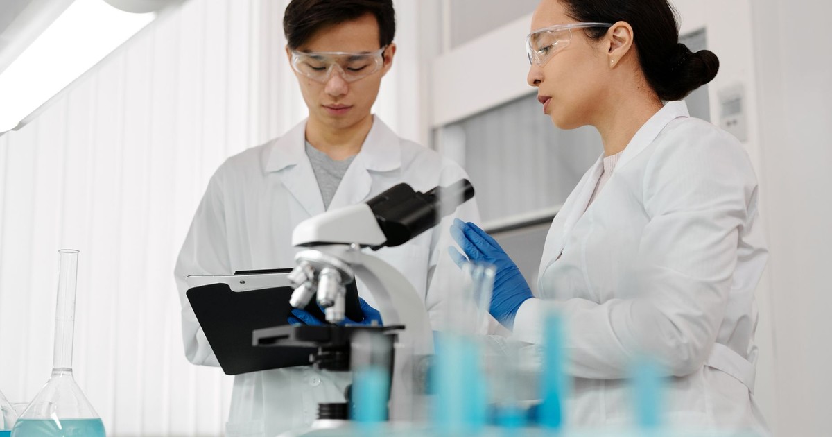 Asian scientists in lab coats discussing research with a microscope in a laboratory setting.