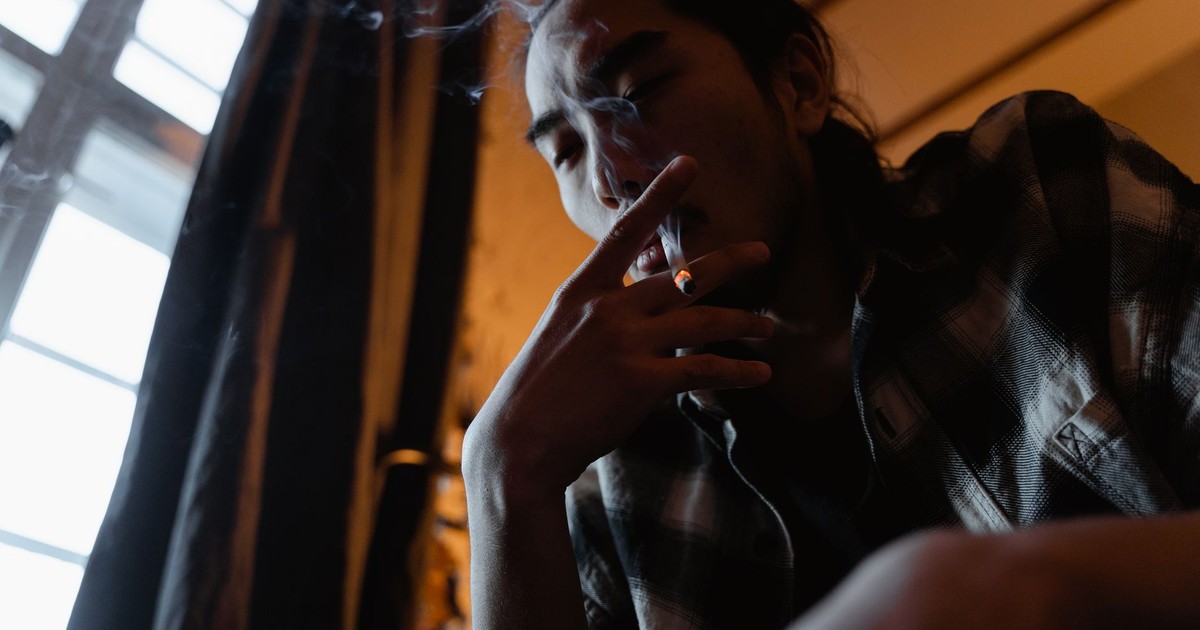 A man deep in thought while smoking a cigarette indoors, low lighting.