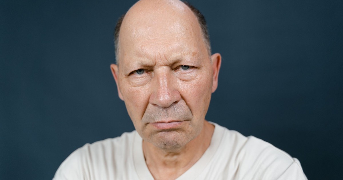 Portrait of a serious senior man in a white shirt against a blue background.
