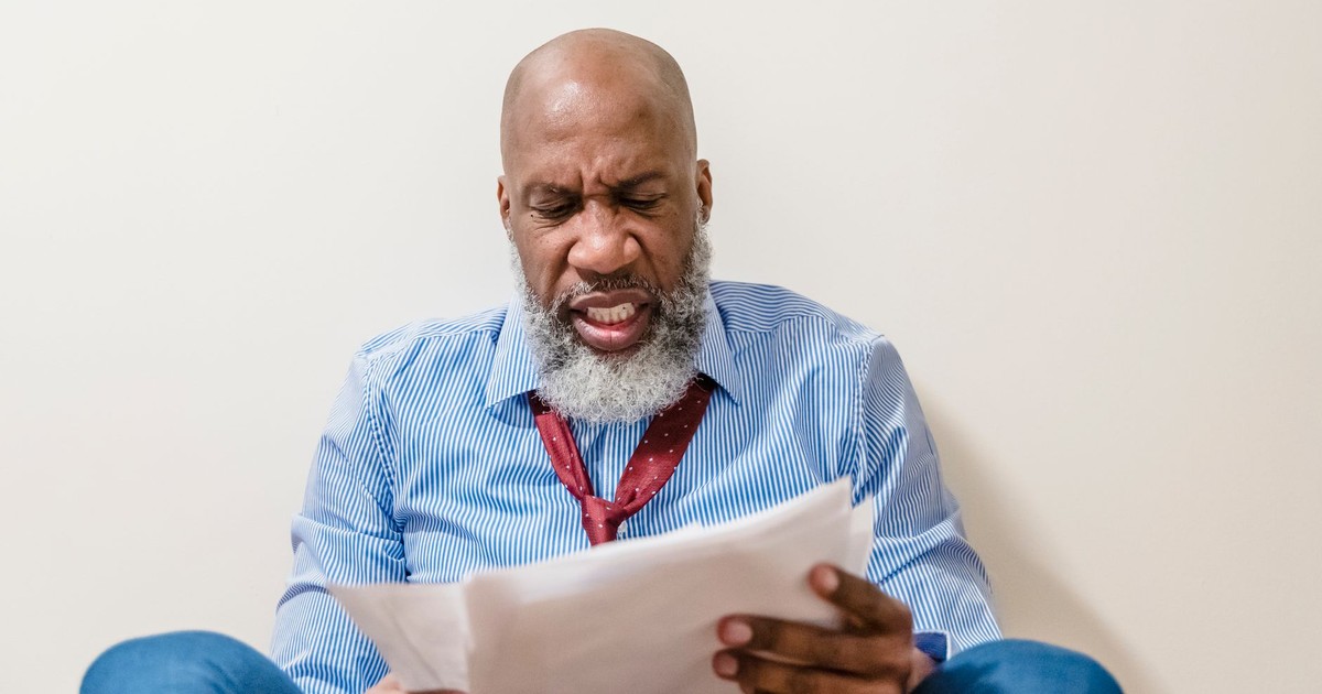 Bald African American man looking stressed while reading documents indoors.