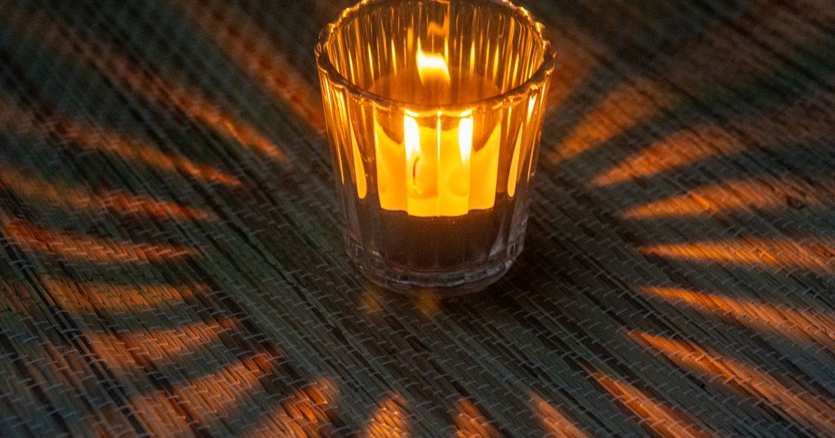 A single wax candle burns with radiant light, casting dramatic shadows.