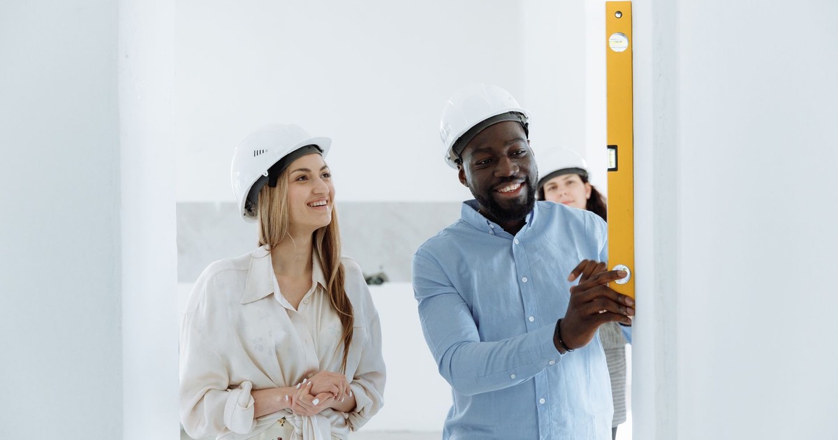 Couple in hard hats using a bubble level during new home construction. Bright indoor setting.