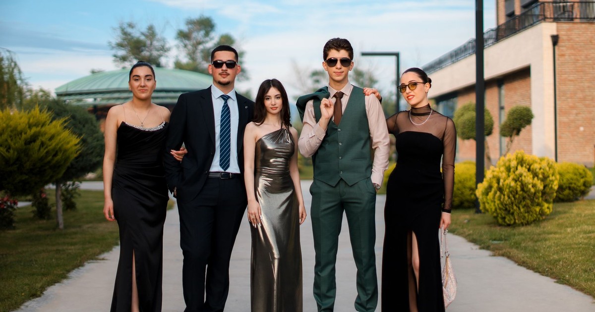 A stylish group of five adults in formal attire posing outdoors on a sunny day.