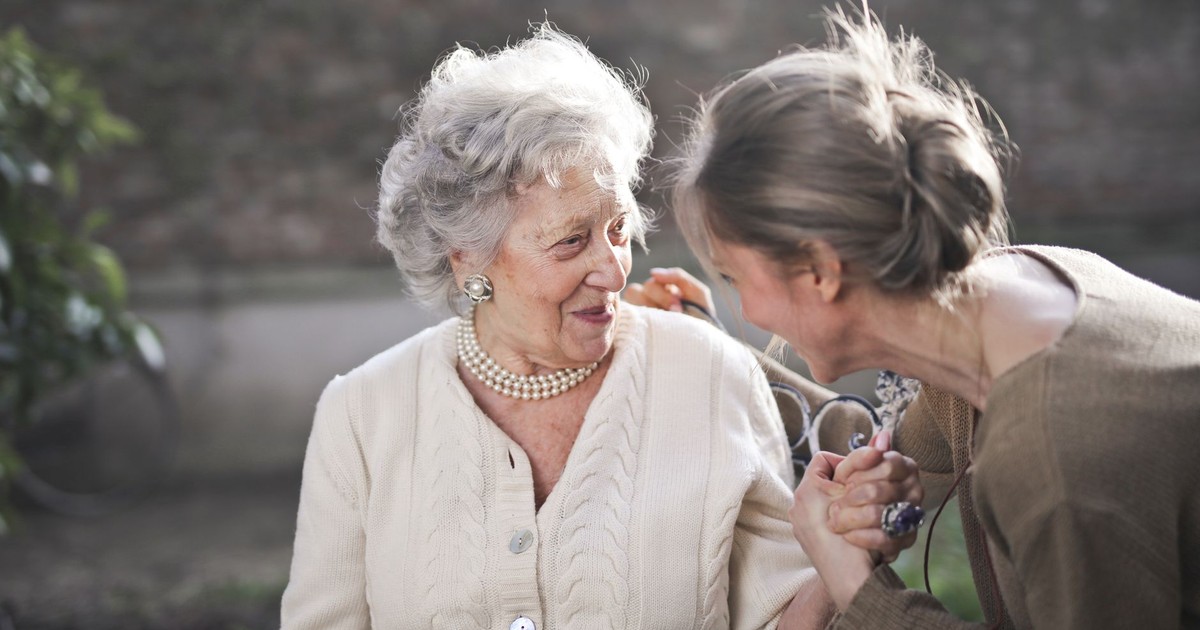 Joyful interaction between an elderly woman and her granddaughter in a sunny outdoor setting.