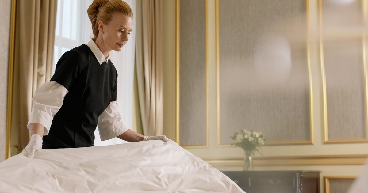 A professional housekeeper fixes a bed in a luxurious hotel room.