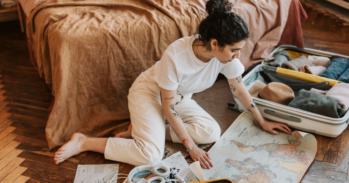 Young woman planning a travel route indoors, surrounded by luggage and a map.