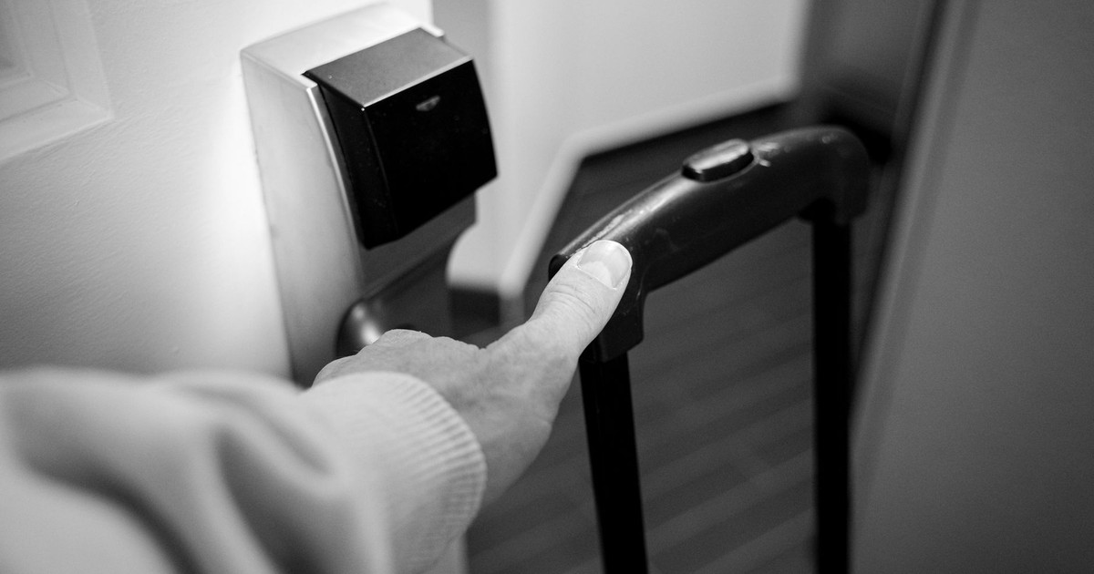 A monochrome photograph of a hand opening a hotel room door with a luggage handle.