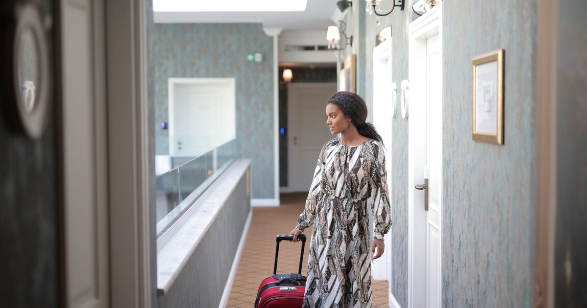 A woman walks with luggage through a stylish hotel corridor, embodying travel elegance.