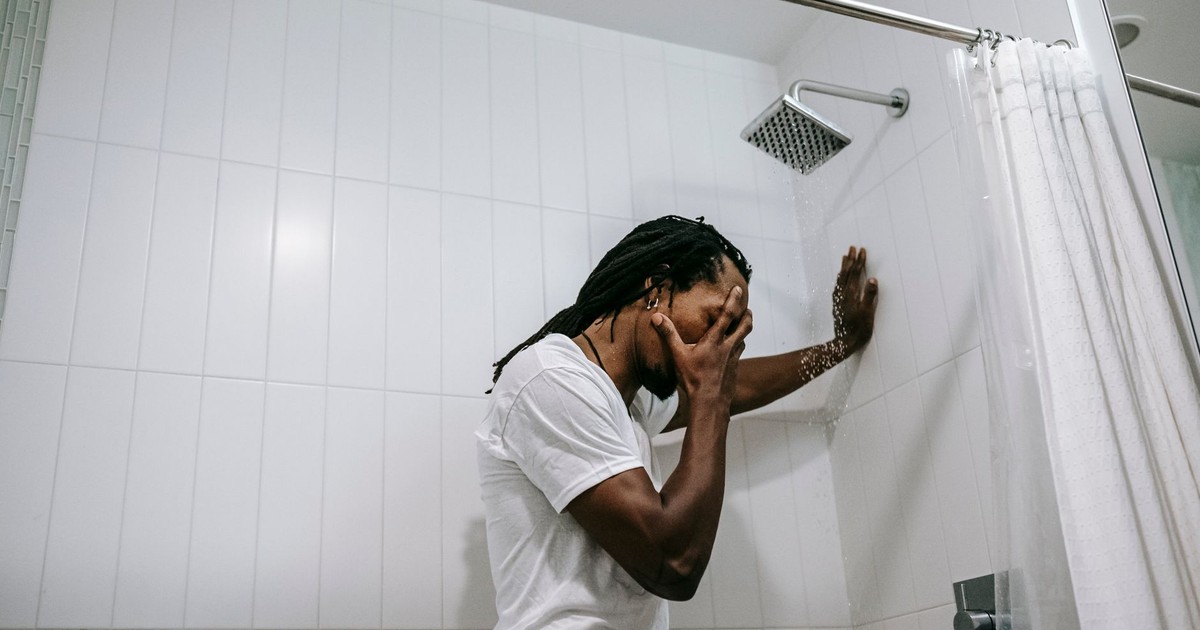 Side view depressed preoccupied African American male in white shirt covering face with hand in anxiety in bathroom