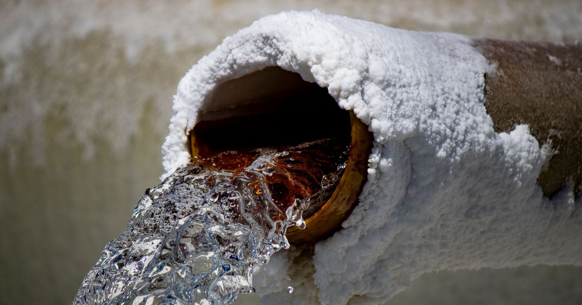 Close-up of water flowing from a rusty pipe with salt deposits, capturing motion and texture.