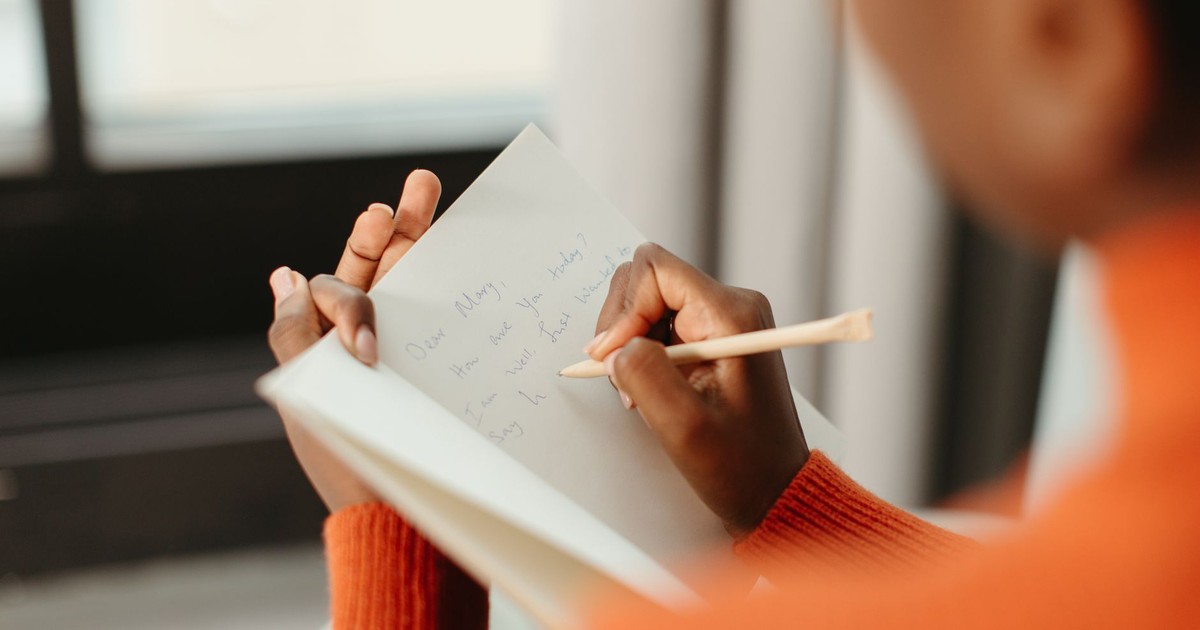 A woman writing a close-up letter in a notebook with a pencil and a blurred background.