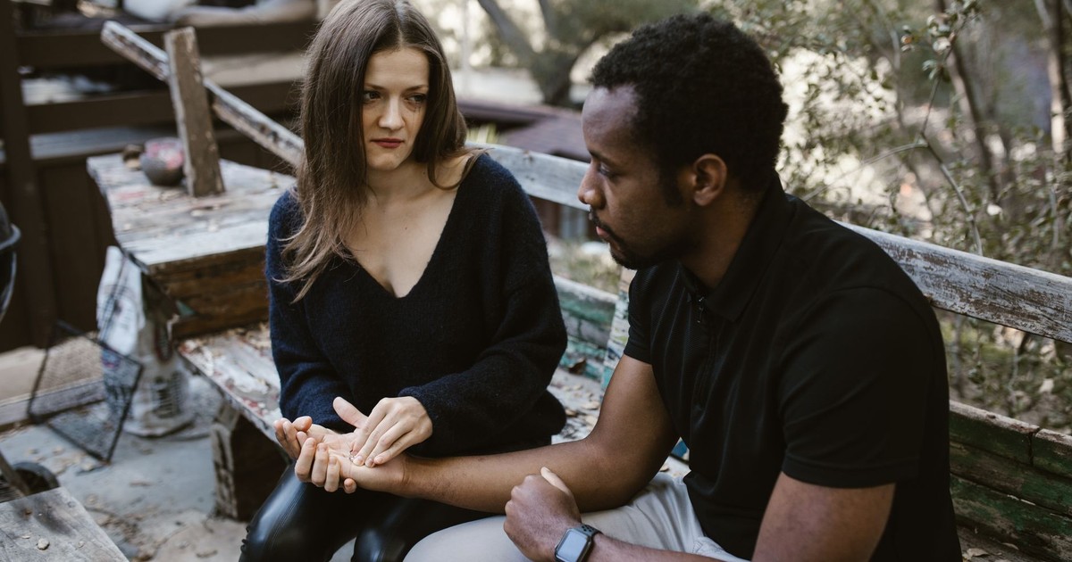 A couple in an emotional conversation on a rustic outdoor bench, conveying tension and concern.